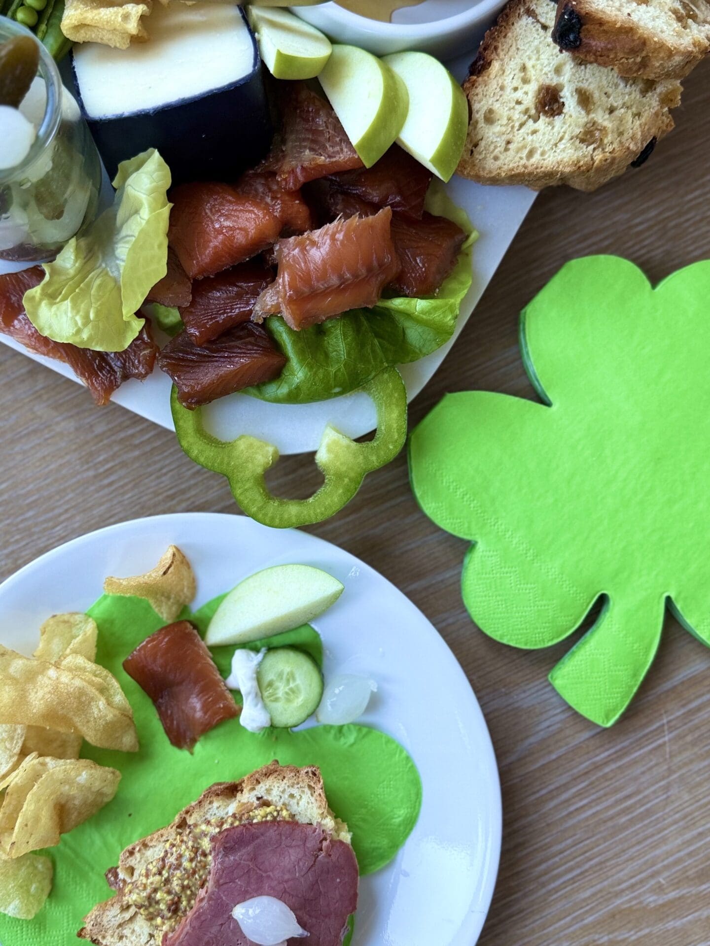 IMG_4834 A St Patrick's Day Charcuterie Board is seen along with an individual plate containing a selection of items from the board. A green shamrock shaped napkin is seen to the side of the photo.