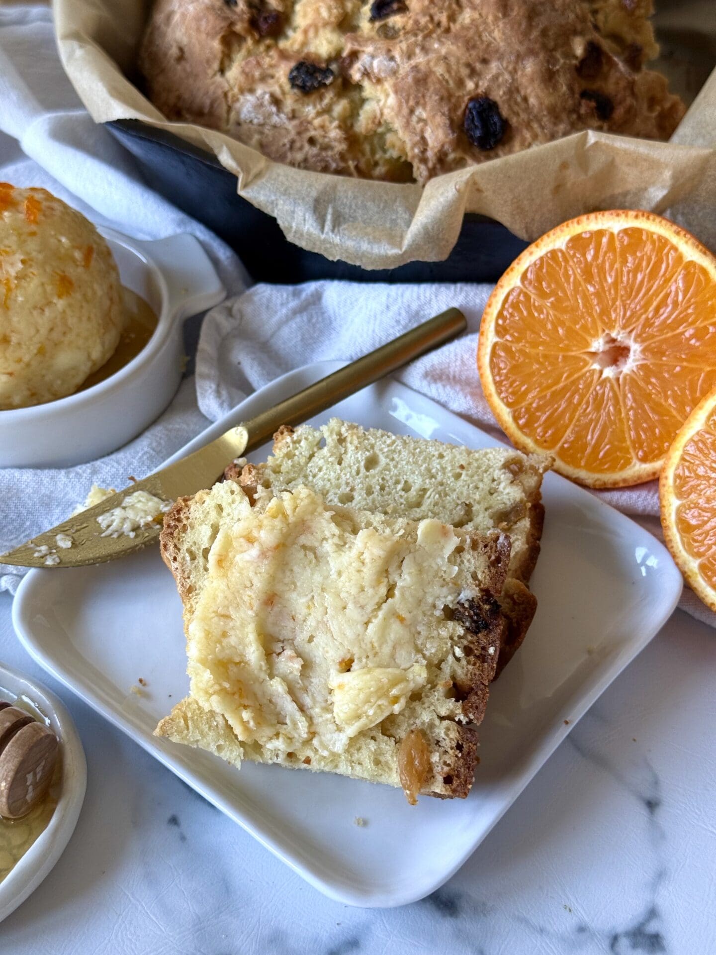 IMG_4848 Homemade Orange and Honey Butter is slathered on slices of freshly baked Irish soda bread. A loaf of the soda bread can be seen in a cast iron skillet in the background. Fresh oranges and a honey dipper complete the image.
