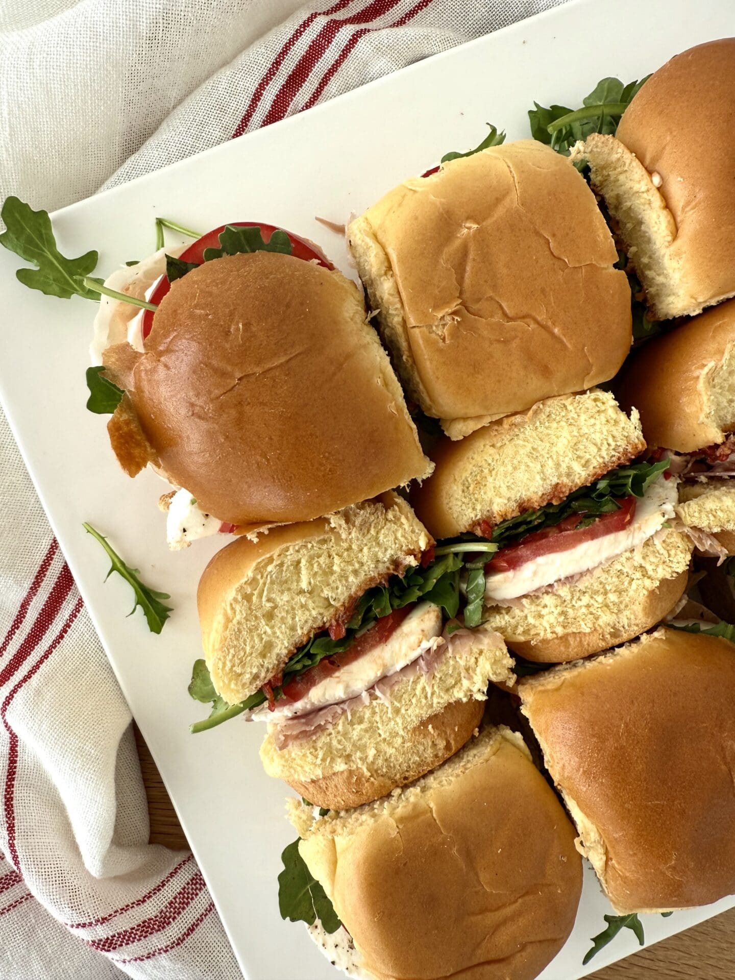 IMG_5051 Half of a platter of Italian Antipasto Sandwich Sliders is seen from above. Some of the sliders have been turned on their sides, revealing their fillings of prosciutto, mozzarella, basil, tomato, arugula and roasted red pepper spread.