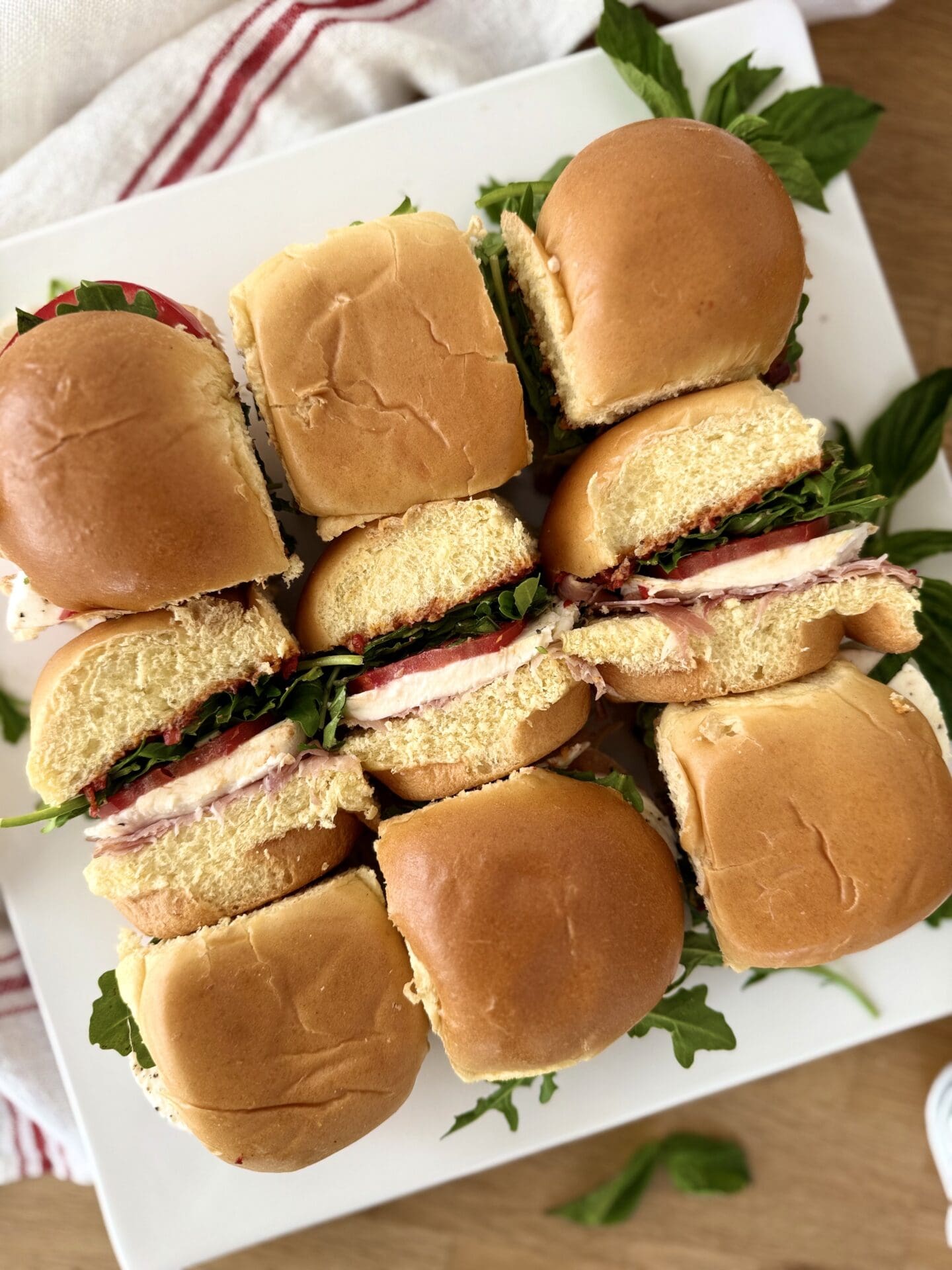 IMG_5062 A platter of nine Italian Antipasto Sliders , arranged in 3 rows, is seen from above. The sliders in the centre row have been turned on their sides so you can see that they are stuffed with prosciutto, fresh mozzarella, tomatoes, basil and arugula.