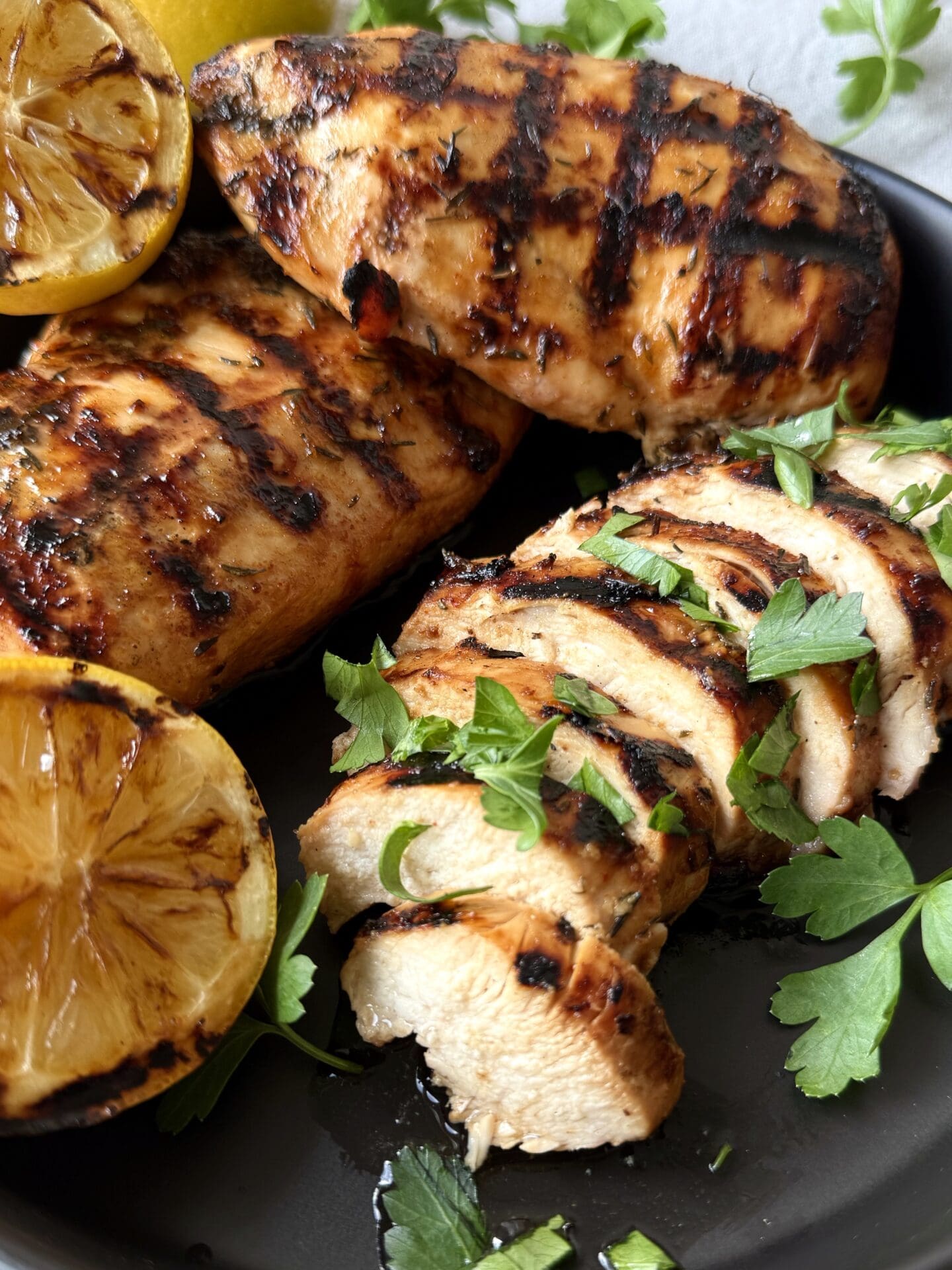 IMG_5142 Sweet and Tangy Marinated Grilled Chicken is seen on a black platter with grilled lemon wedges and fresh parsley.