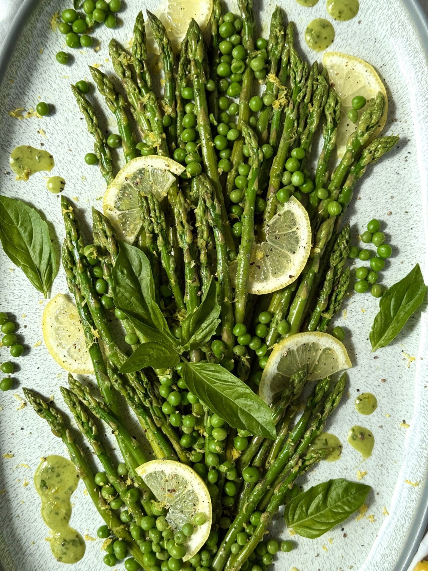 Lemon Basil Asparagus and Peas side side is seen close up, from above.  The image shows the garnishes of lemon slices, fresh basil leaves, lemon zest and black pepper.