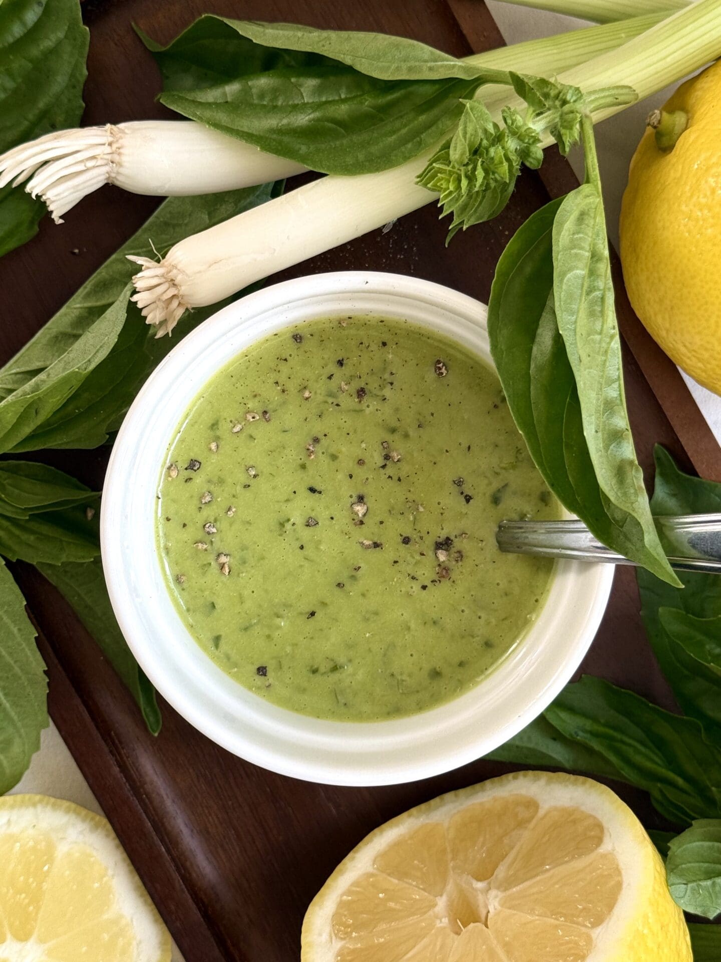 IMG_5409 A bowl of Homemade Lemon Basil Dressing sits on a dark wood tray, surrounded by lemons, fresh basil leaves and green onions.