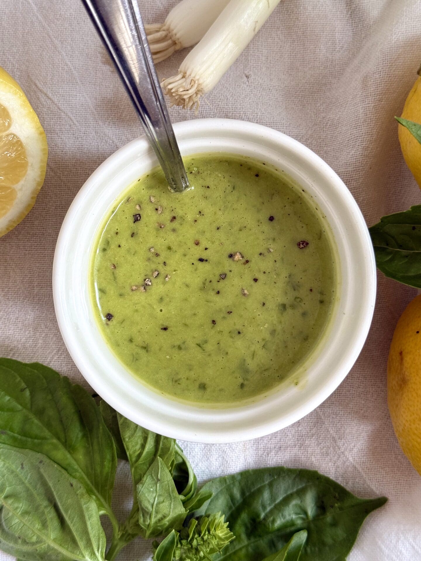 IMG_5426 A bowl of Lemon Basil Vinaigrette is seen from above surrounded by fresh basil, lemons and spring onions.