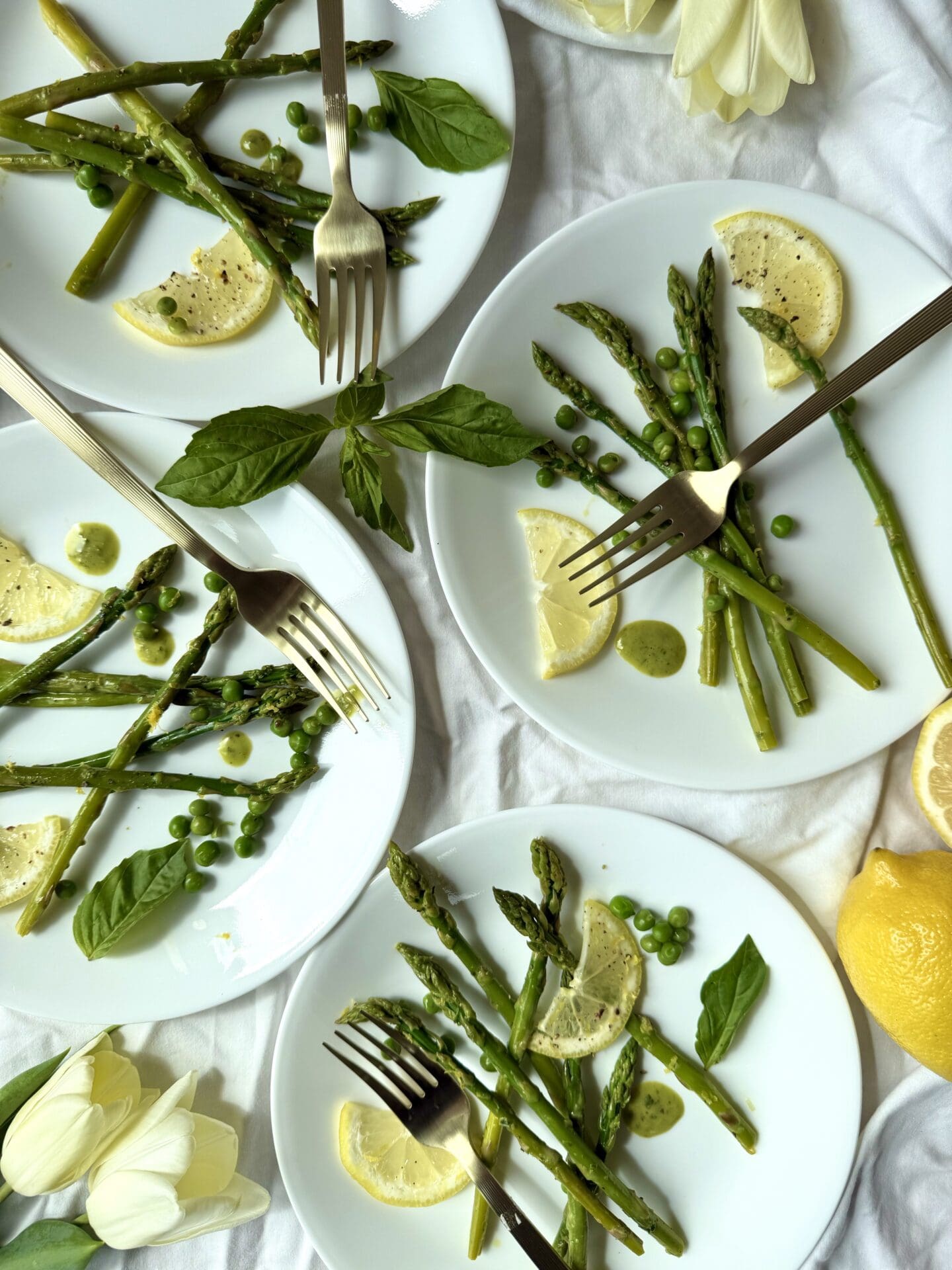 IMG_5443 Four individual plates containing servings of Lemon Basil Asparagus with Peas are seen from above, surrounded by lemons, fresh basil and tulips.