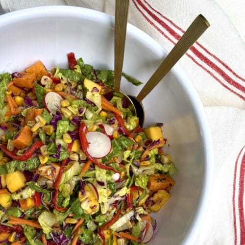 A bowl of colourful Mexican Chopped Salad is seen from above in a white bowl, surrounded by a red and white striped cloth.