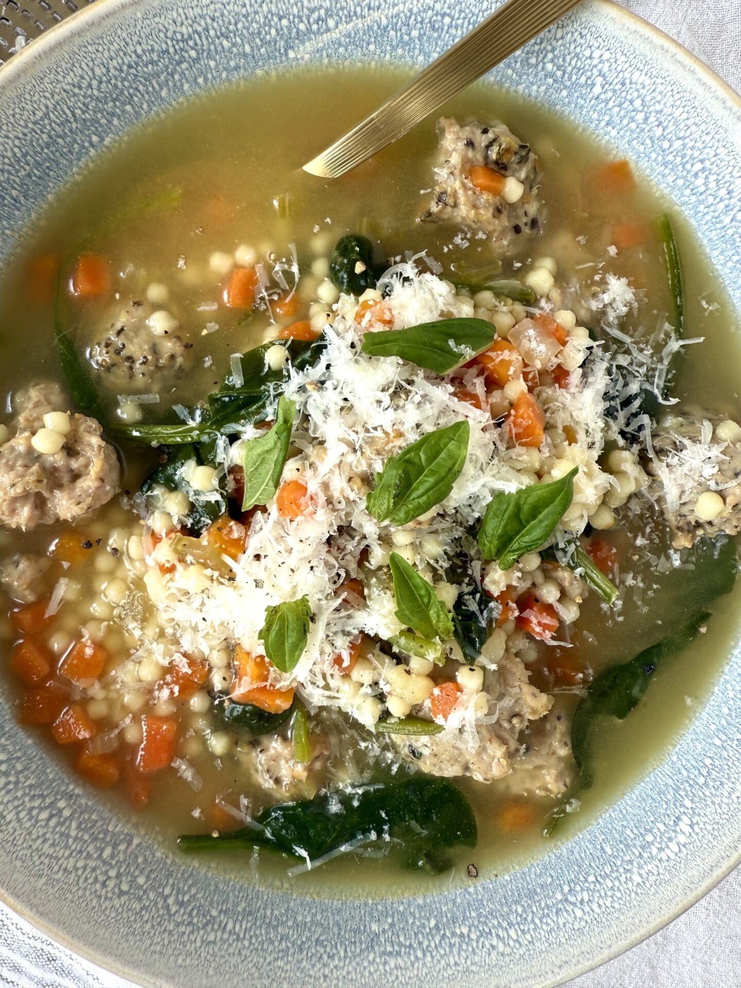 IMG_5683 A bowl of Healthier Italian Wedding Soup is seen from above, garnished with freshly grated parmesan cheese and tiny green basil leaves.