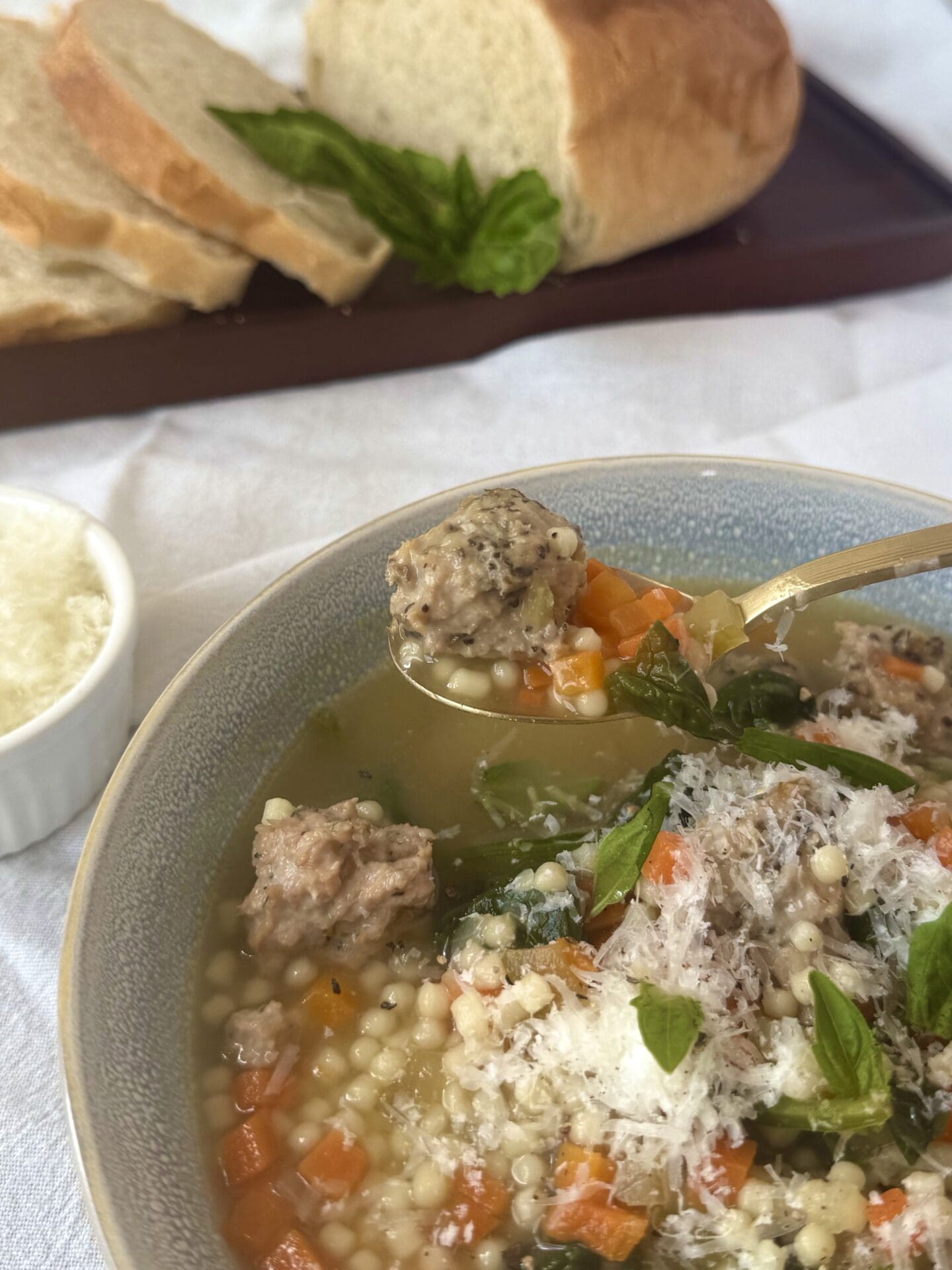 IMG_5691 A spoon lifts a roasted turkey meatball from a bowl of Healthier Italian Wedding Soup. Fresh bread and a bowl of freshly grated pecorino Romano cheese are seen in the background.