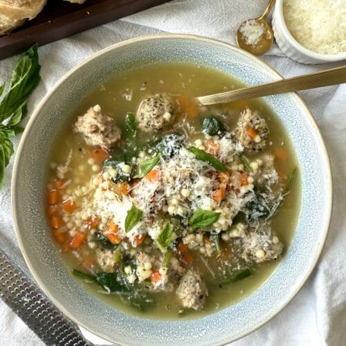 A bowl of Healthier Italian Wedding Soup is seen from above, laden with turkey meatballs and finely chopped vegetables, and garnished with freshly grated Pecorino Romano cheese.