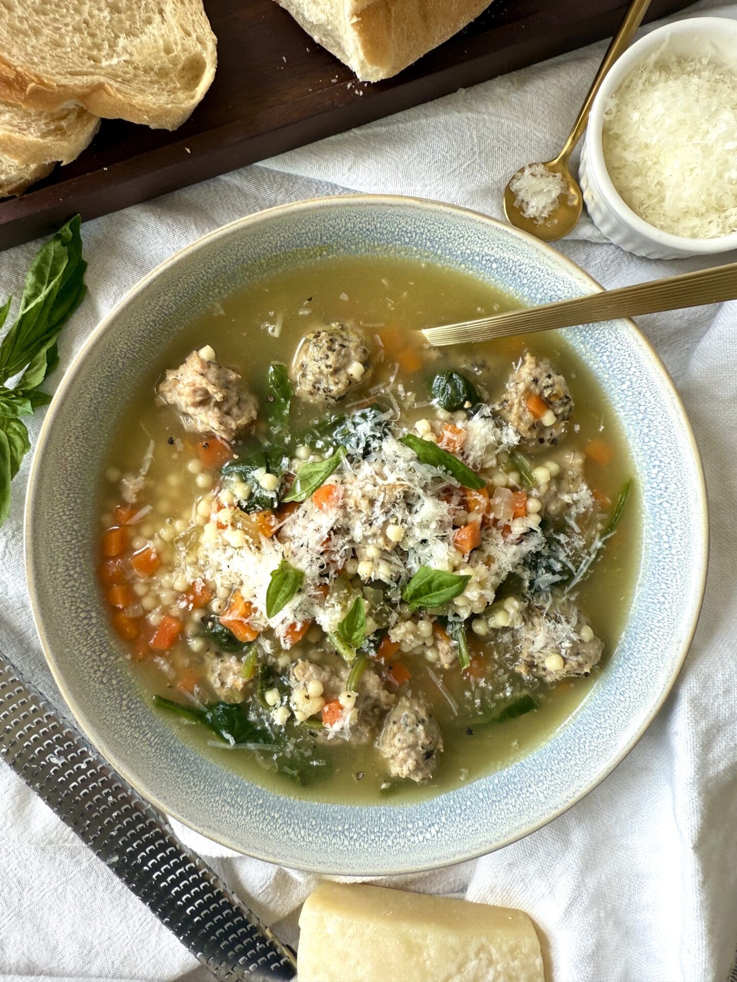 A bowl of Healthier Italian Wedding Soup is seen from above, laden with turkey meatballs and finely chopped vegetables, and garnished with freshly grated Pecorino Romano cheese.