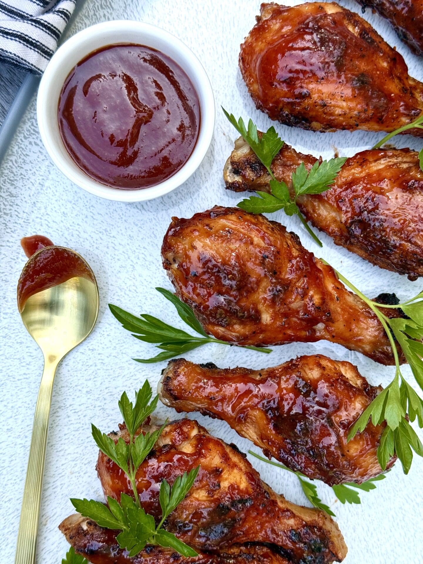 IMG_5935 A platter of Smokey Sweet Grilled Chicken Legs is seen from above garnished with a dish of homemade barbecue sauce and fresh parsley.