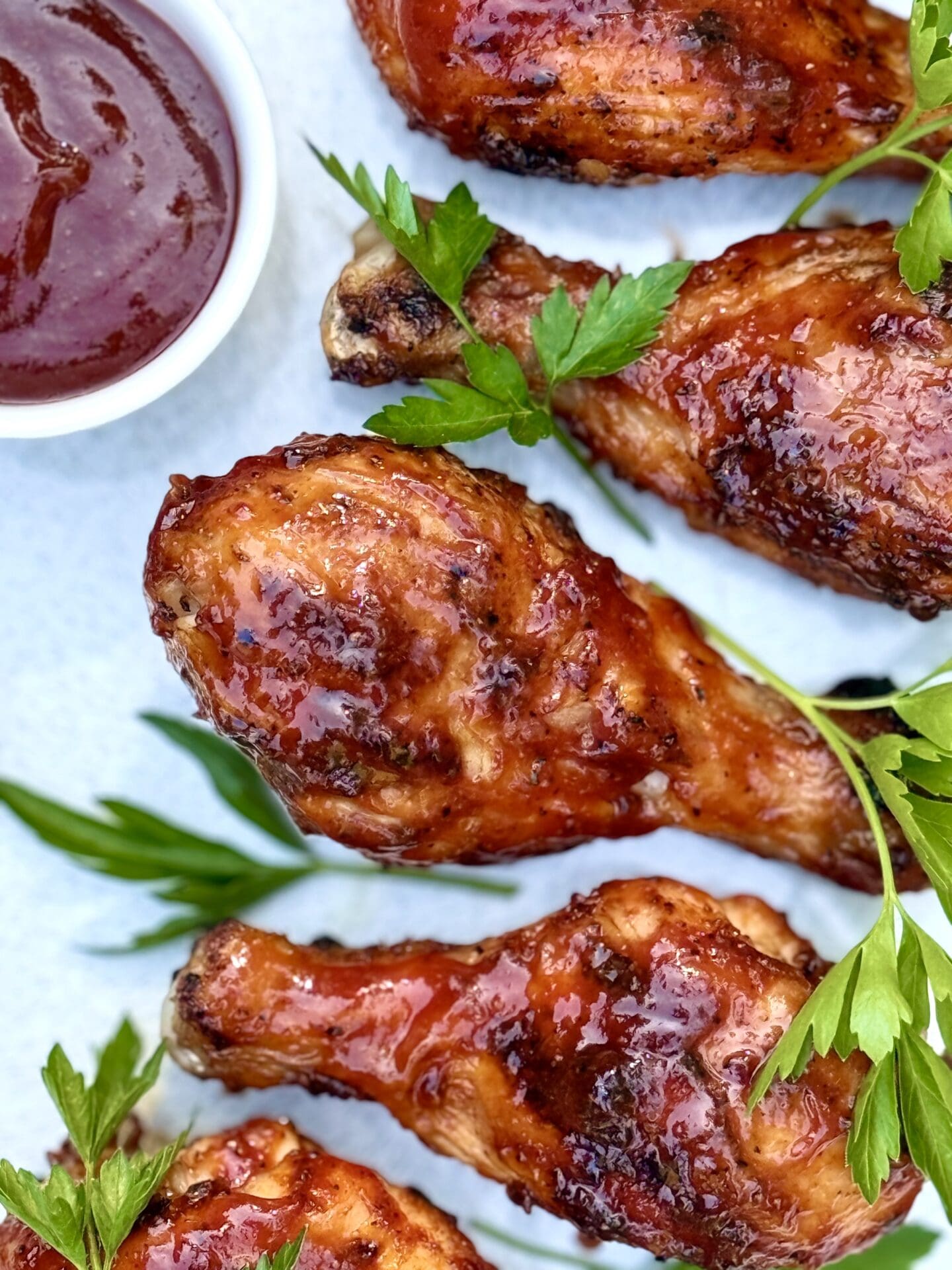 Smokey Sweet Grilled Chicken Legs are seen from above, on a platter, garnished with a small dish of barbecue sauce and a sprinkling of fresh parsley.