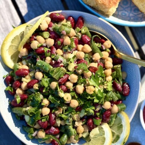 Marinated Three Bean Salad is seen from above on a picnic table in the late afternoon light, garnished with lemon slices