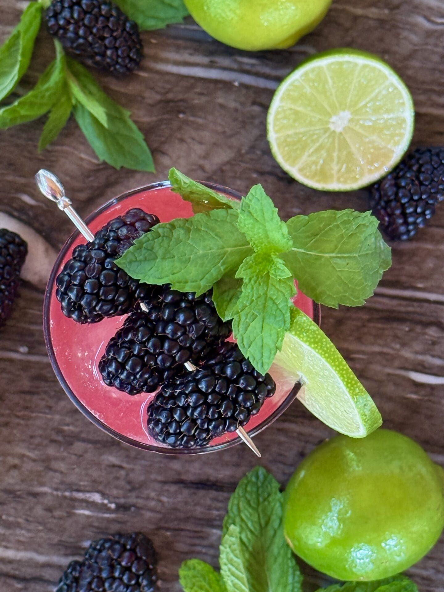 IMG_6470 A glass of Blackberry Mojito Mocktail is seen from above garnished with a cocktail pick strung with plump blackberries, a lime wheel and sprigs of fresh mint.