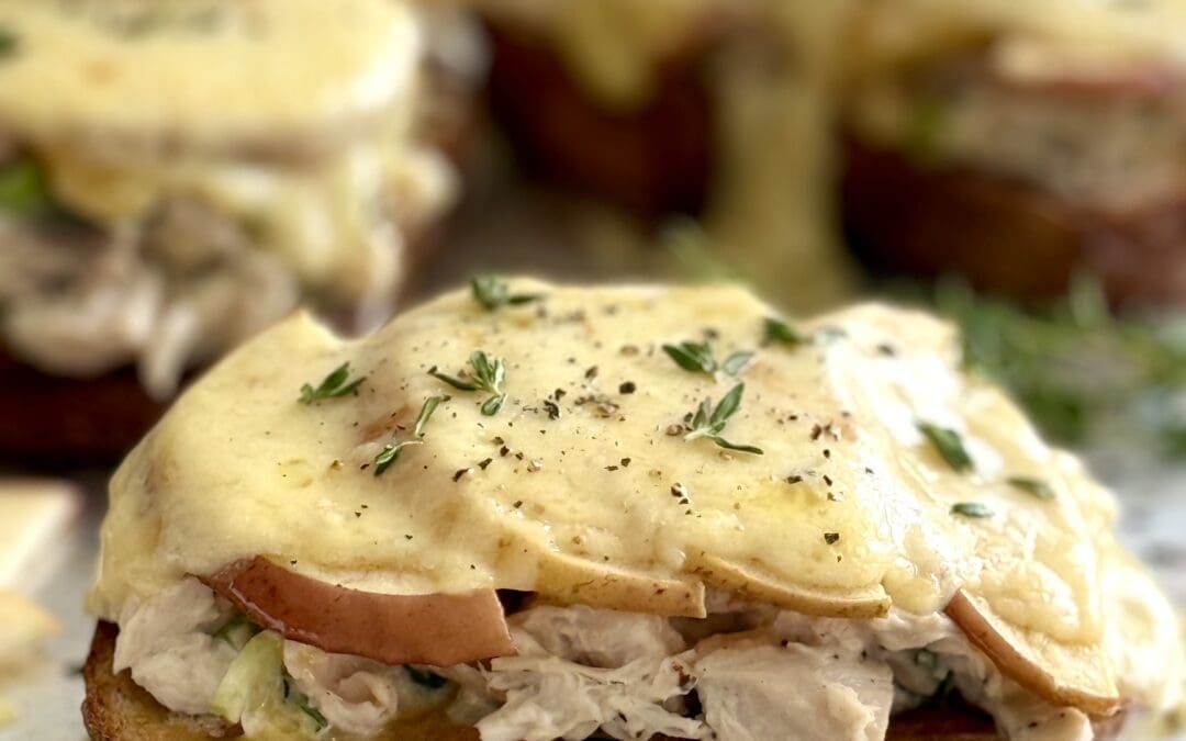 Chicken and Apple Melts with Smoked Cheddar are seen hot from the oven with melting cheese dripping down over the edges of the sandwiches.