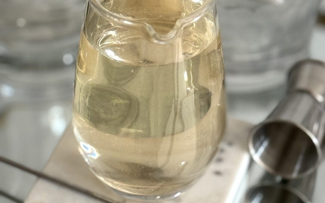 A glass of homemade simple syrup sits on a sparkling bar cart, surrounded by a jigger, stirring spoon and other bar implements.