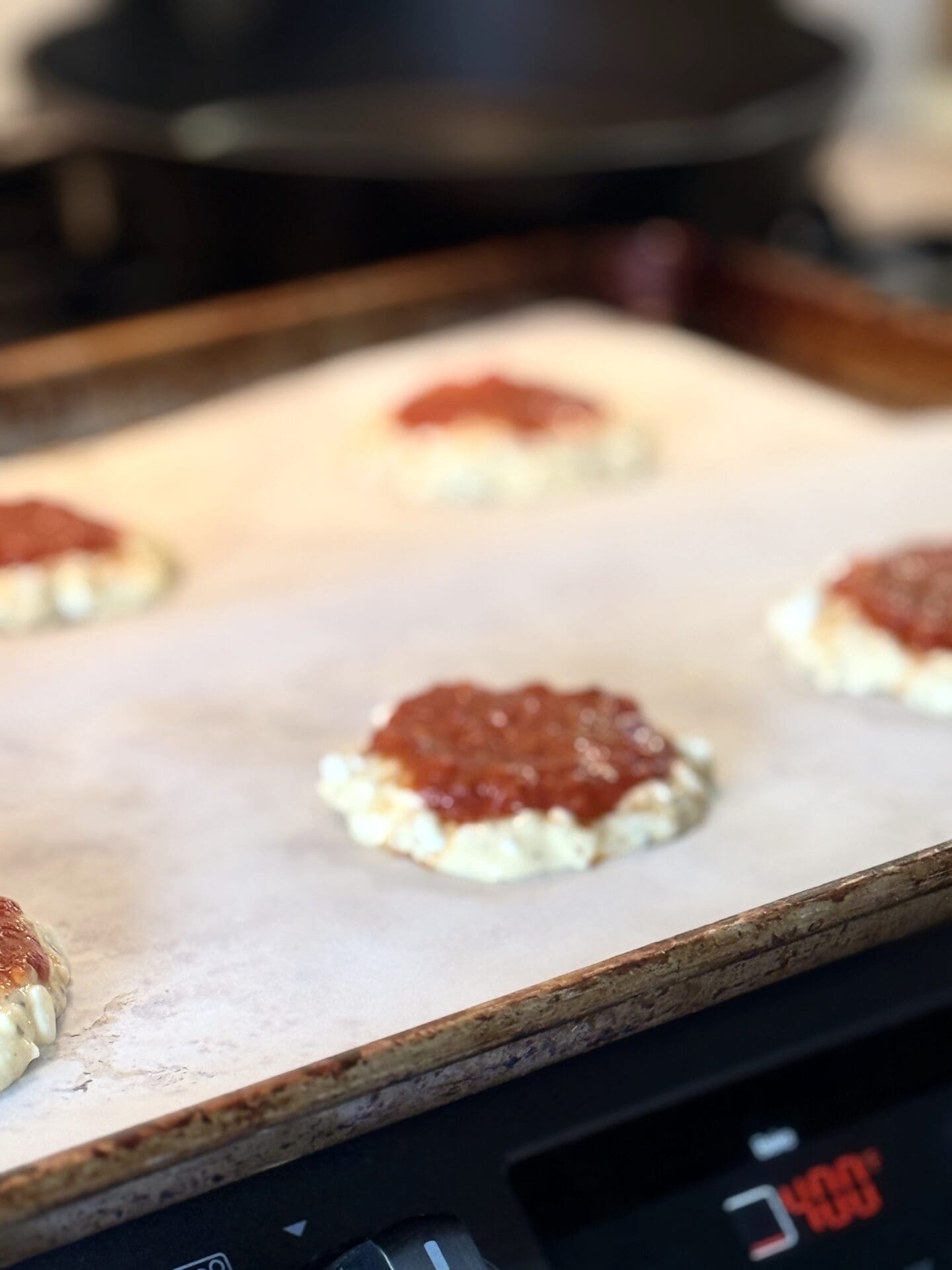 A process shot of a baking sheet showing the unbaked cottage cheese pizza bun batter shaped into buns and topped with marinara sauce.