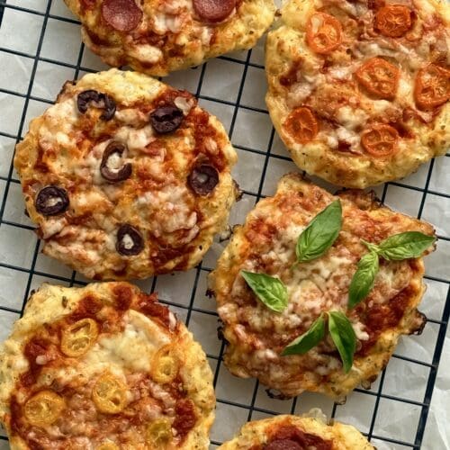 Cottage Cheese Pizza Buns featuring an assortment of toppings are seen from above, fresh from the oven, cooling on a black wire rack.