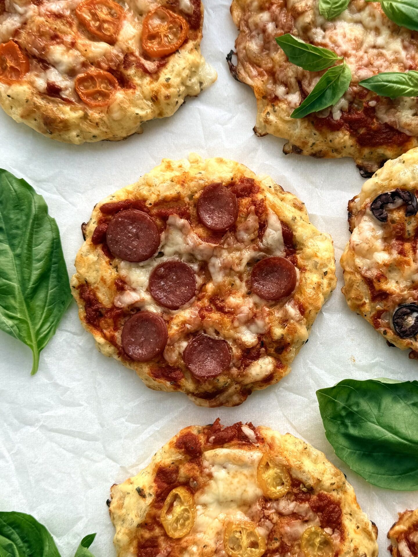Baked cottage cheese pizza buns are seen from above on a baking sheet.  The pizza in the centre is topped with pepperoni, whereas the surrounding pizza buns feature an assortment of colourful vegetables.