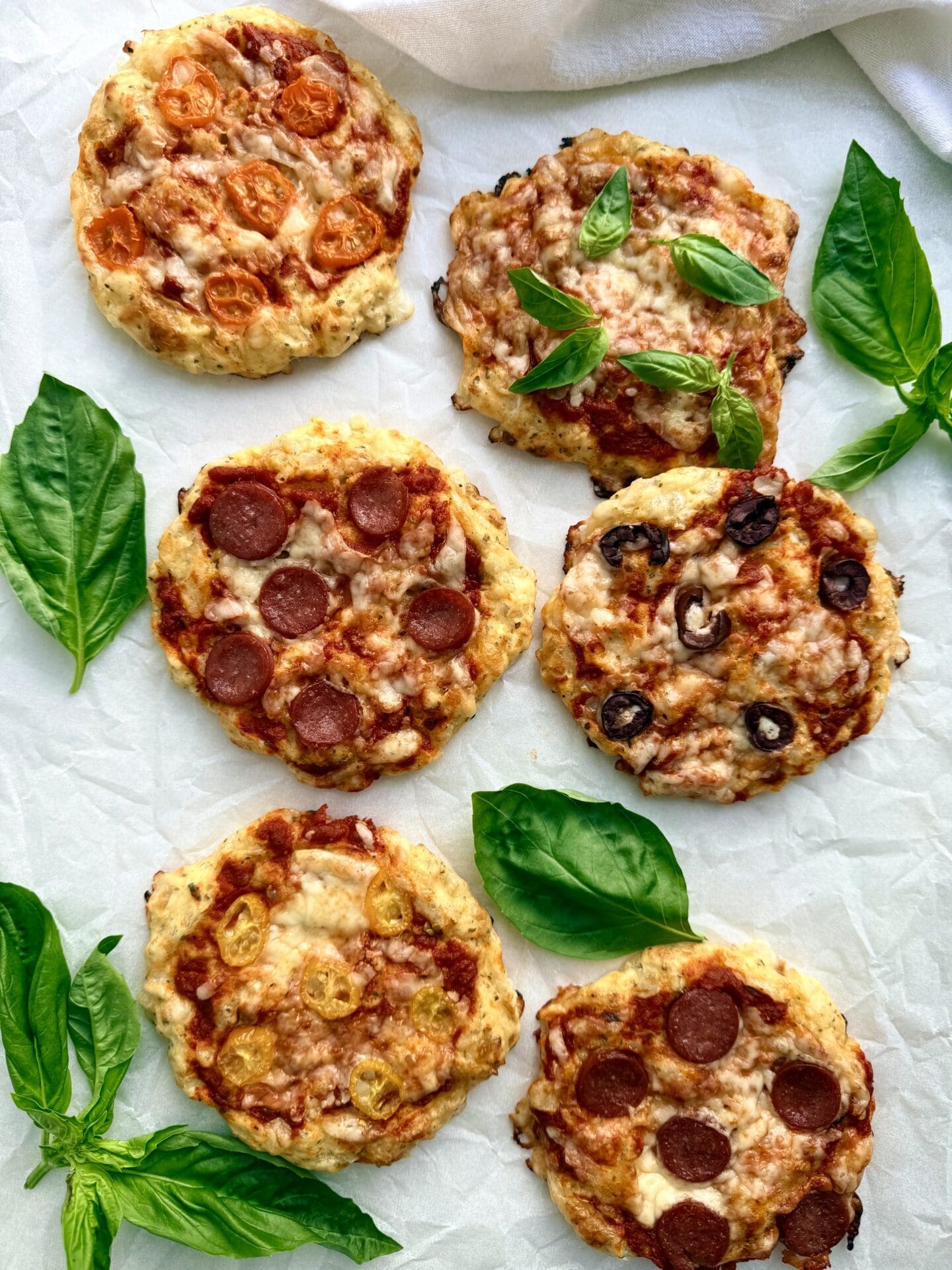 Freshly baked cottage cheese pizza buns are seen from above, surrounded by fresh basil leaves.