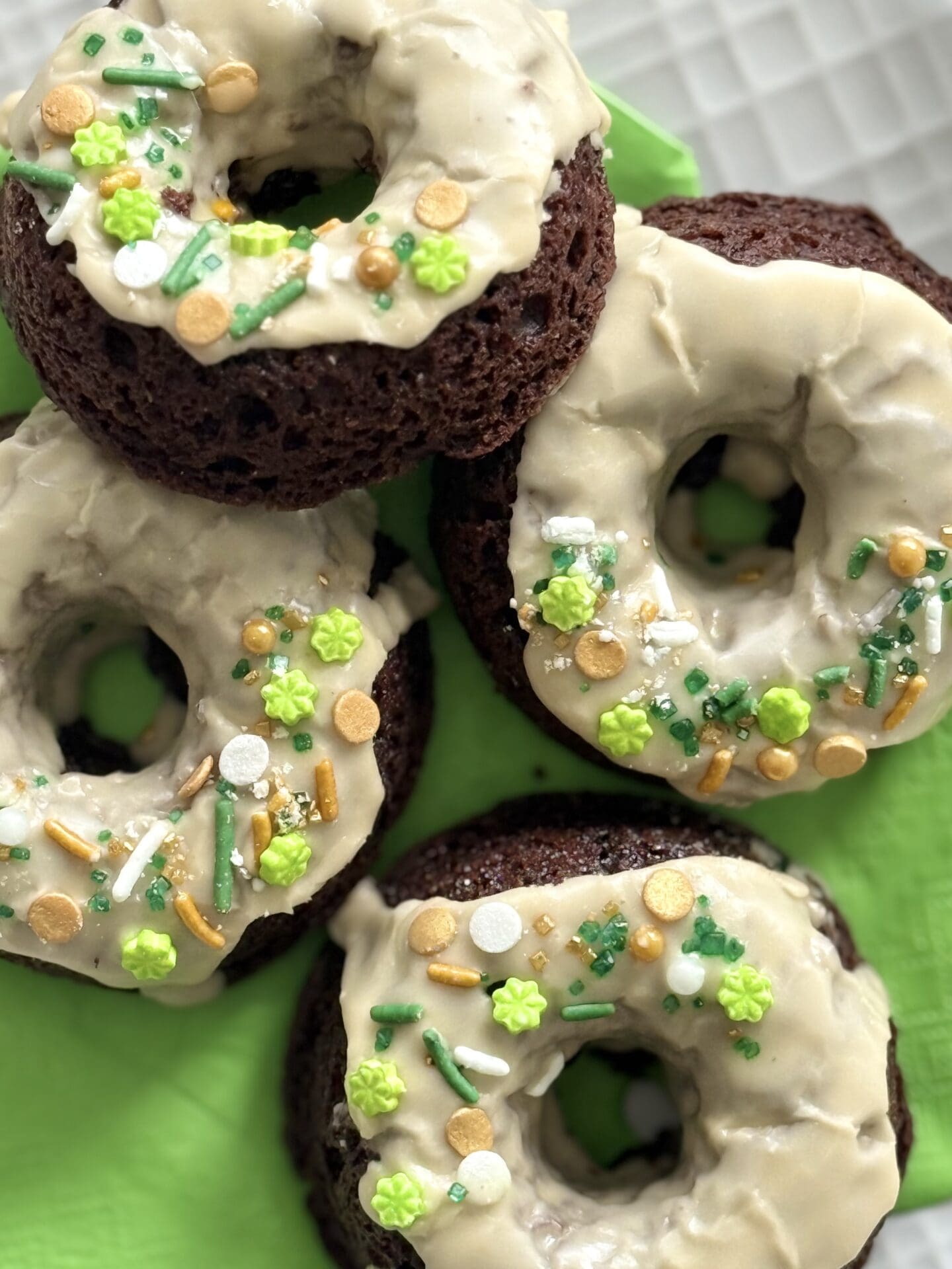 A group of four Baileys Glazed Chocolate Donuts sits on a plate lined with a green napkin.