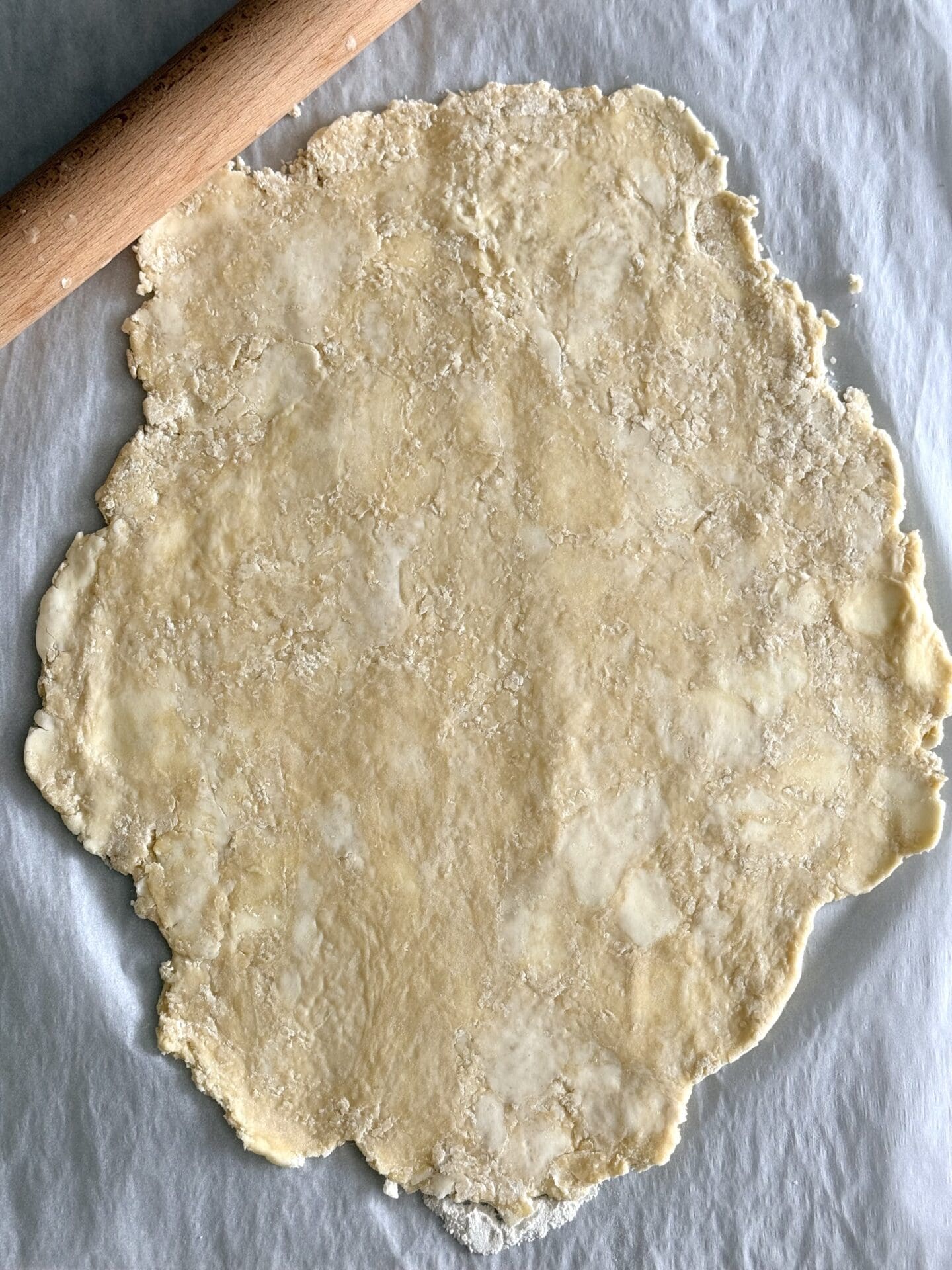 The chilled pastry for butter tarts is rolled out on a sheet of wax paper.  Pieces of butter are still visible in the dough.