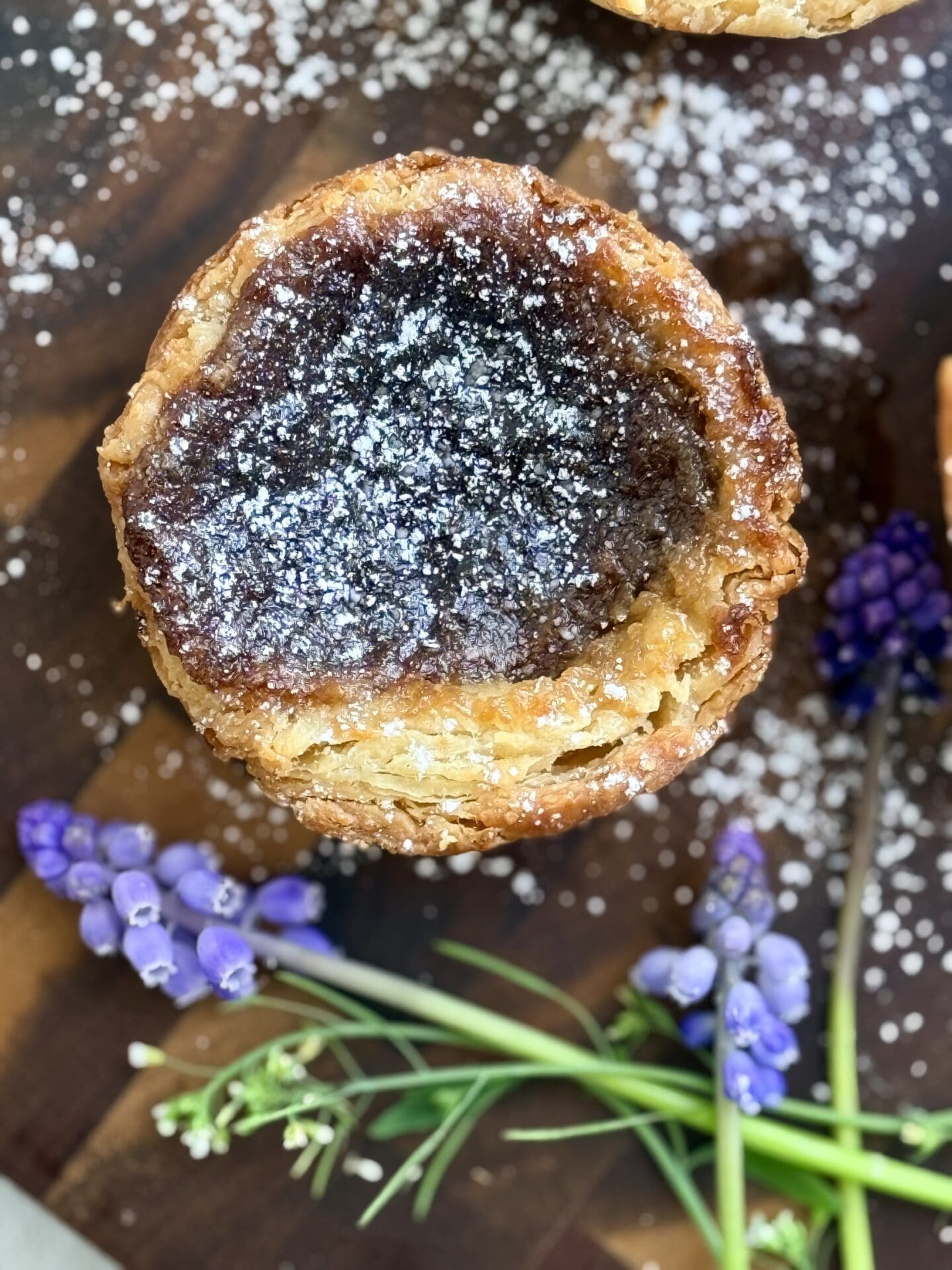 A single butter tarts sits on a wood board, displaying its flaky, golden crust.