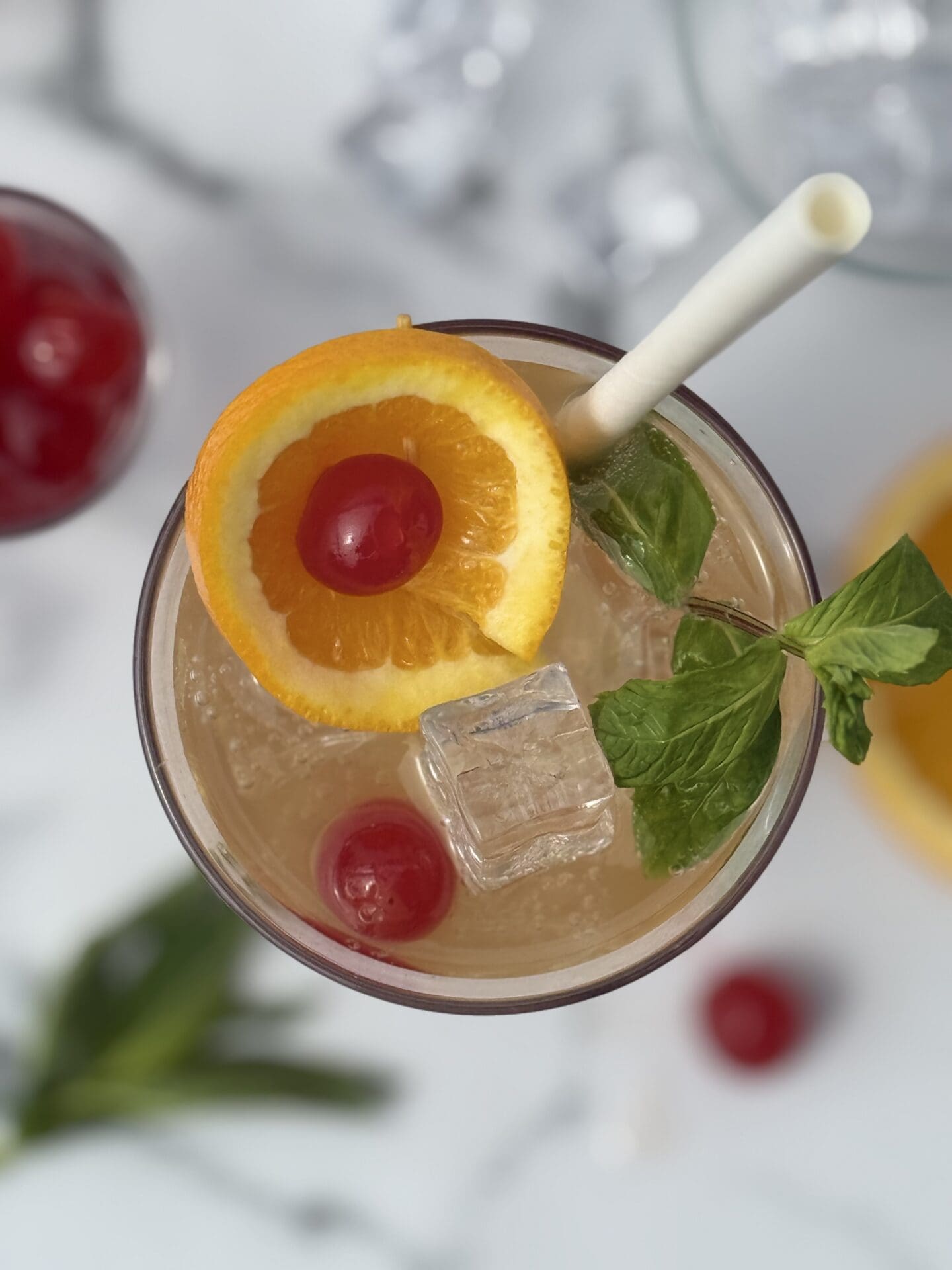 A Shirley Temple drink is seen from above, garnished with an orange slice, maraschino cherries and fresh mint.