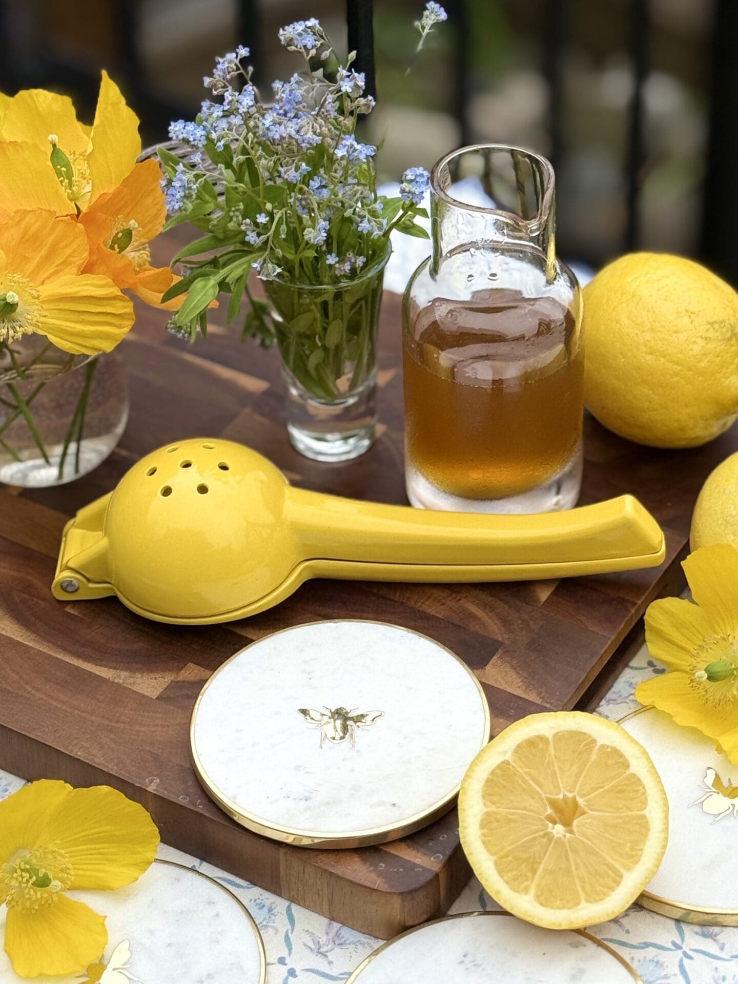 The ingredients for a Bee’s Knees cocktail sit on a wooden board, ready for use.  Honey simple syrup, fresh lemons and spring flowers can be seen.