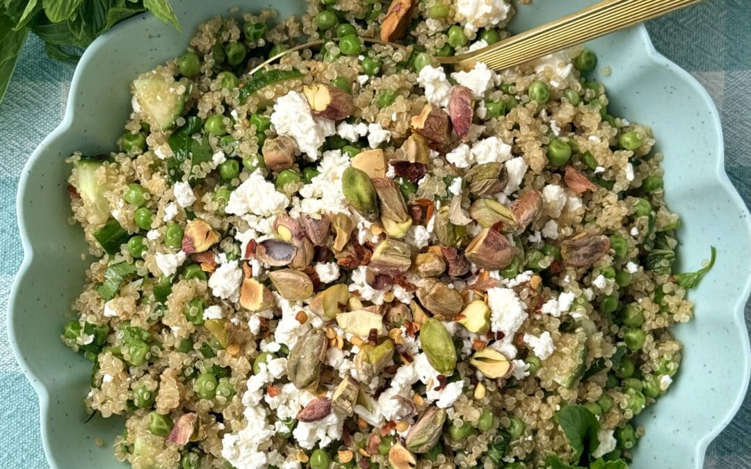 A bowl of Lemony Quinoa Salad with Spring Peas and Pistachios is seen from above, surrounded by fresh mint and lemons.