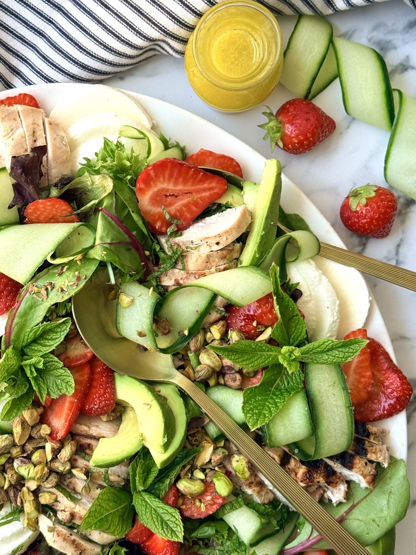 A platter of Strawberry Cucumber Salad with Grilled Lemon Chicken is seen up close, showing off its vibrant mix of fresh summer vegetables, berries and fresh herbs.