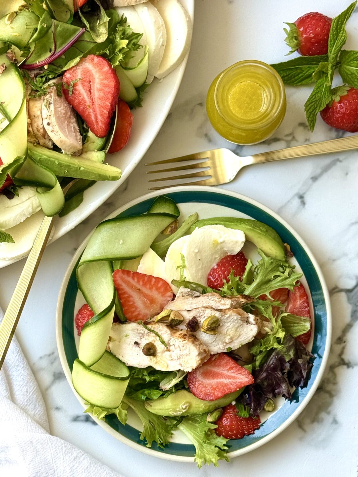 A plate of Strawberry Cucumber Salad with Grilled Lemon Chicken is served from the large platter.  A bottle of homemade lemon dressing and additional whole berries are seen nearby.