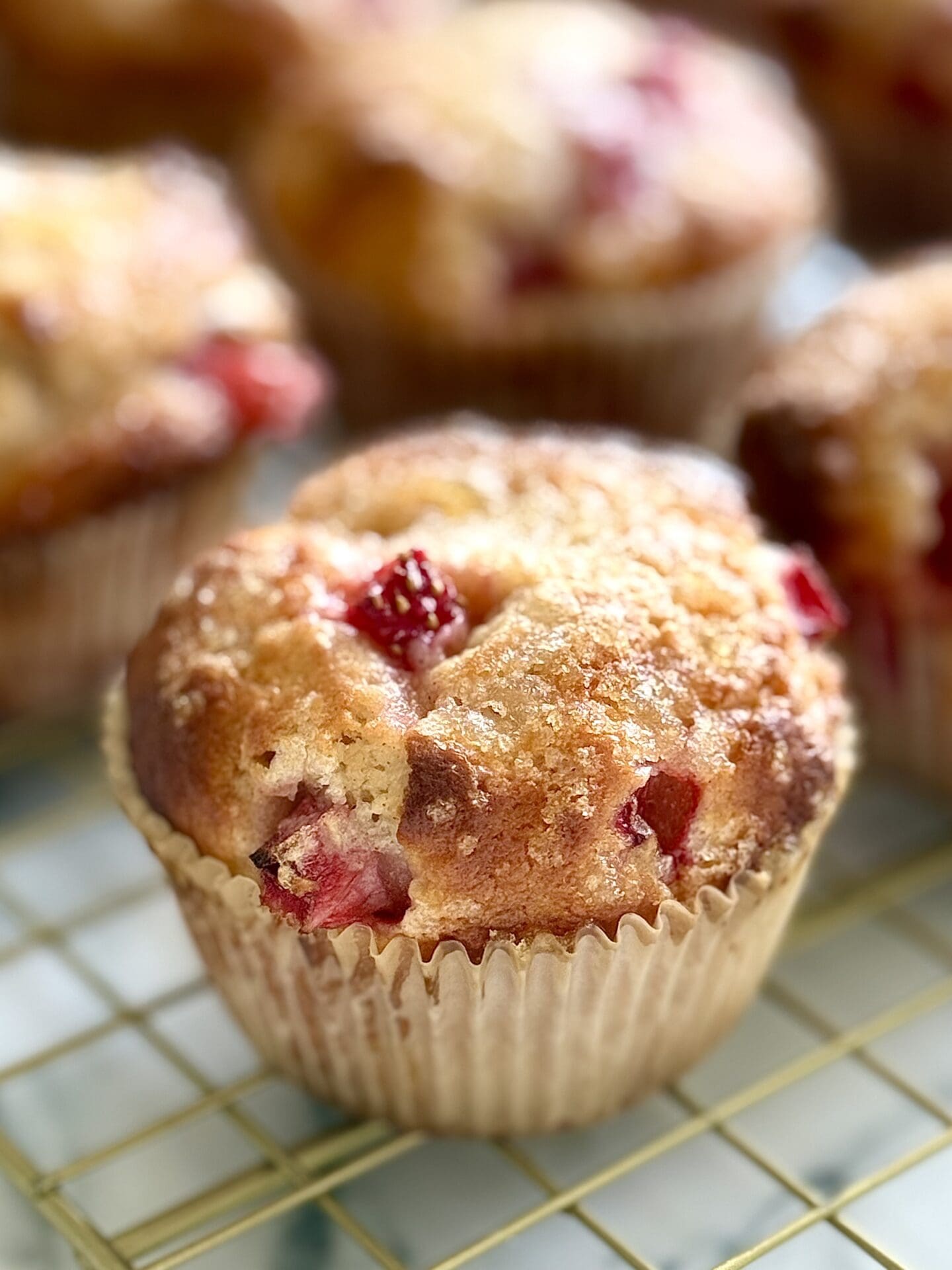A freshly baked strawberry yogurt  muffin is seen close up, showing its crispy lemon sugar coated top, and pieces of juicy strawberry.