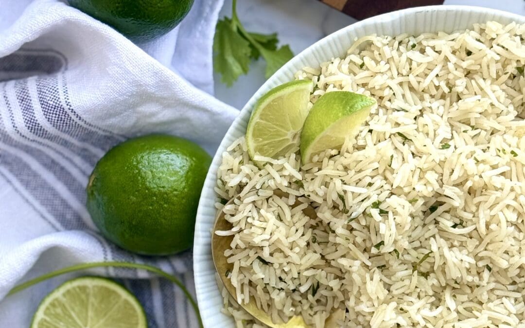 A bowl of cilantro lime rice is seen from above, surrounded by cut limes and fresh cilantro.