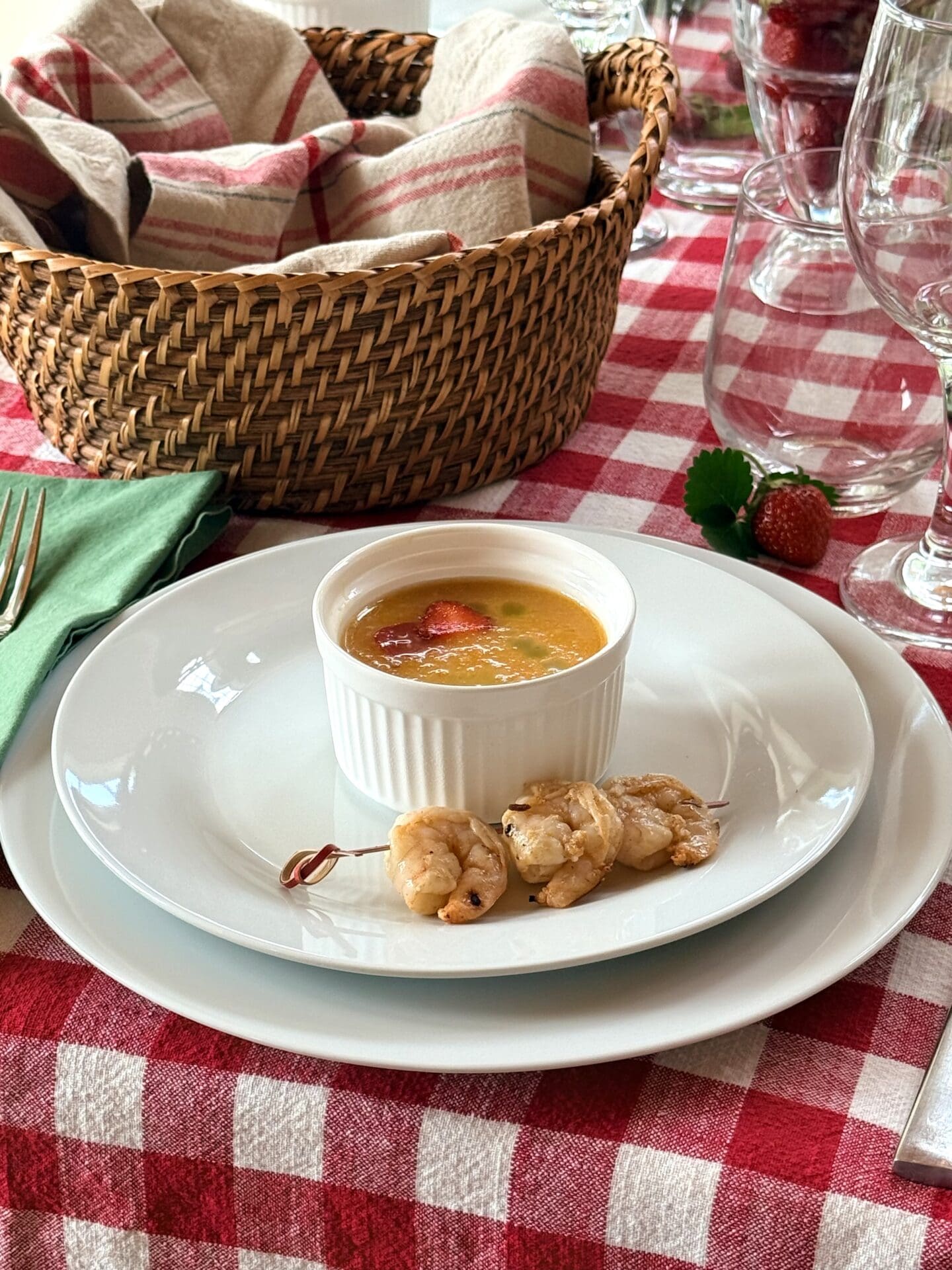 A small bowl of yellow tomato gazpacho is served as a first course alongside a skewer of spicy orange grilled shrimp.