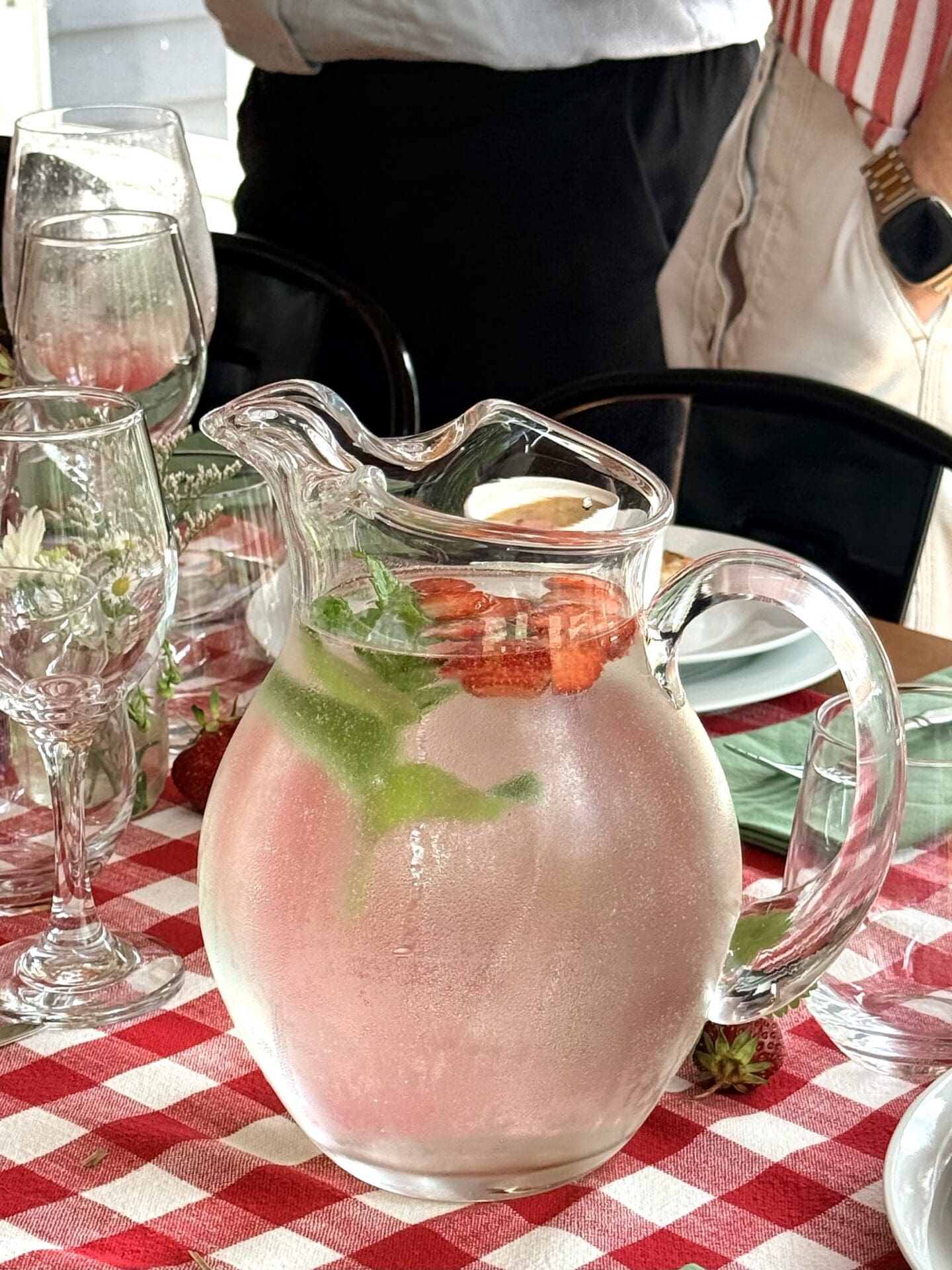 A glass pitcher filled with strawberry and mint ice water rests on a table set for lunch.