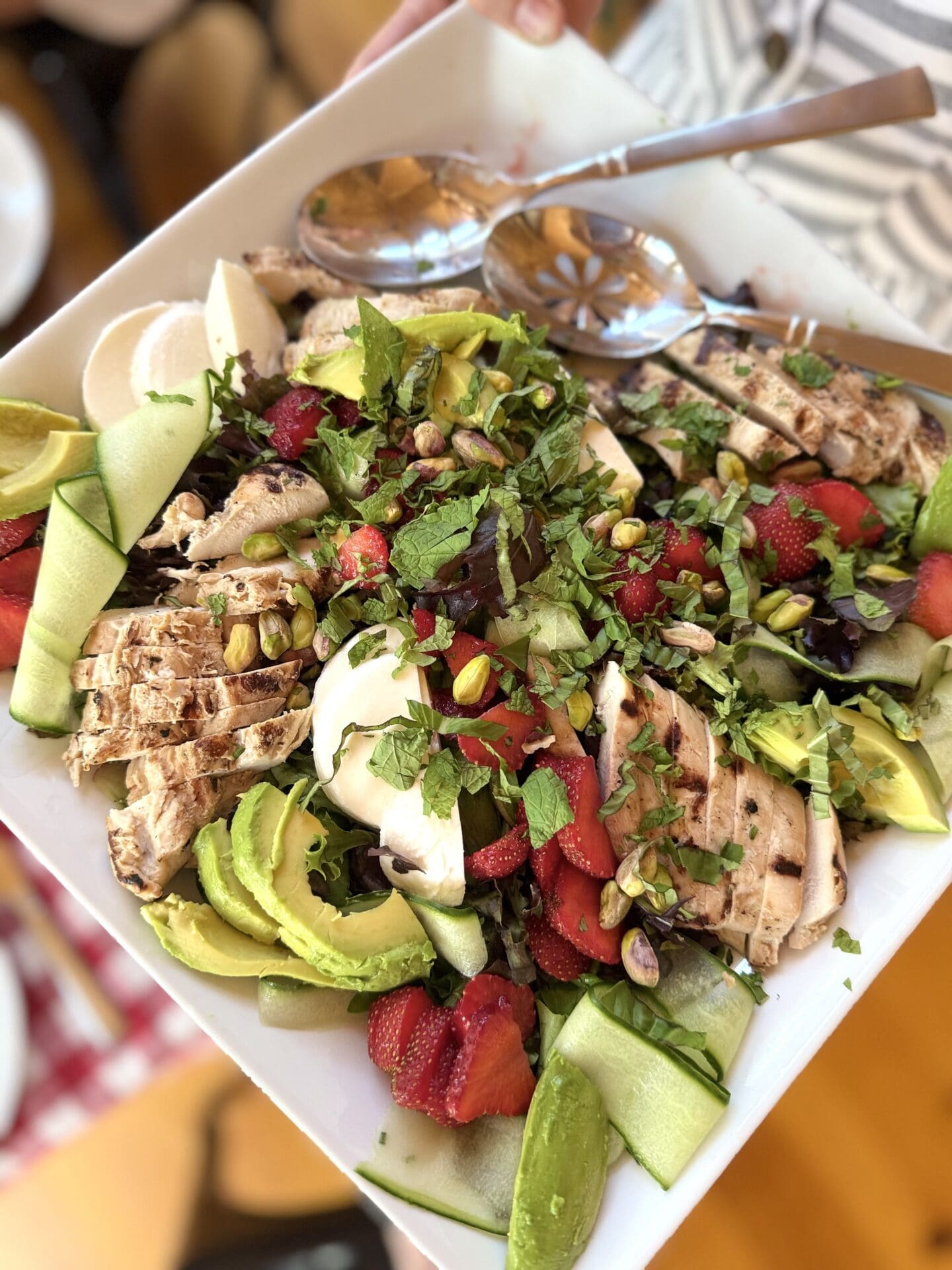 A large platter of Strawberry and Cucumber Salad with Grilled Lemon Chicken is served by a woman in a summer dress.
